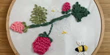 Embroidery combining code-stitched flowers and a hand-stitched bee.